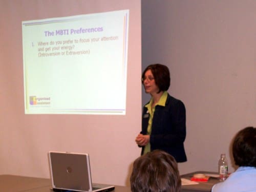 A photo of Janet Barclay delivering a presentation. Background slide reads: The MBTI Preferences 1. Where do you prefer to focus your attention and get your energy? (Introversion or Extraversion)
